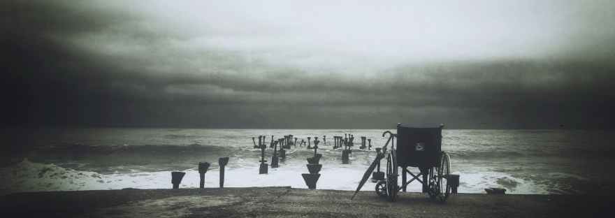 Umbrella and empty wheelchair overlook the ocean on a cloudy day.